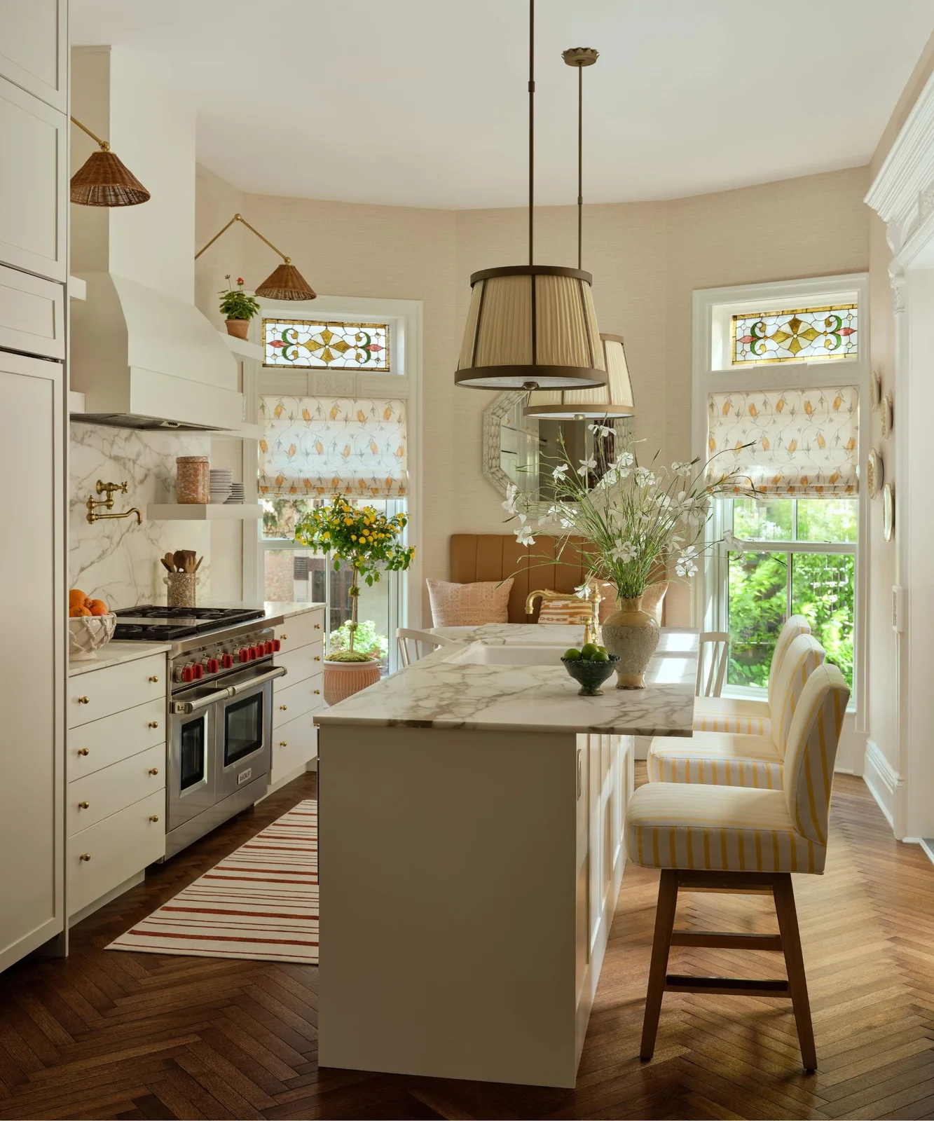 White framed cabinets and a pale island sit beneath pleated pendants beside patterned blinds and stained-glass window details.