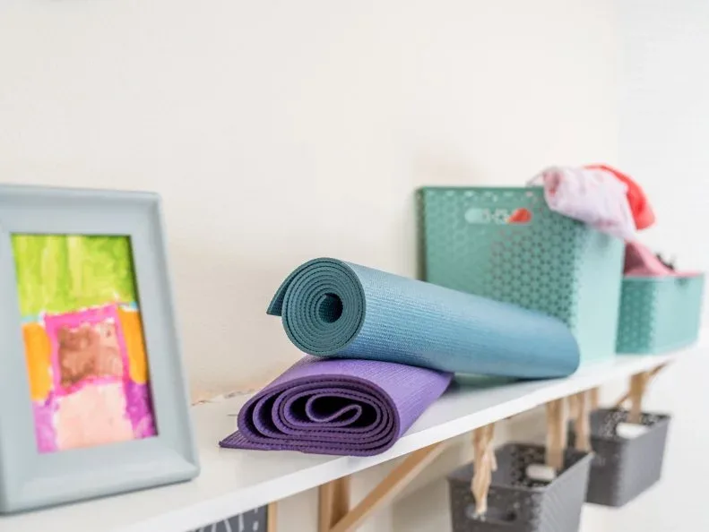 Rolled blue and purple mats beside a colored basket on a white shelf above the coat area.