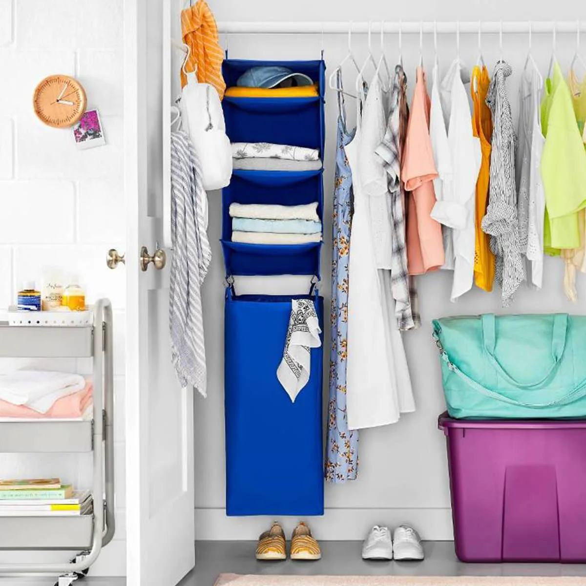 Open closet with a blue fabric hanging organizer, pale clothes, shoes and a purple storage bin