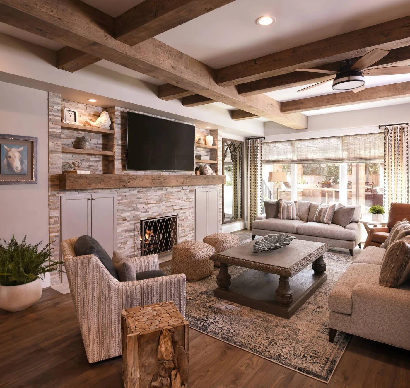 Textured fireplace wall with wooden mantel, television, pale cupboards, open shelves and upholstered seating.