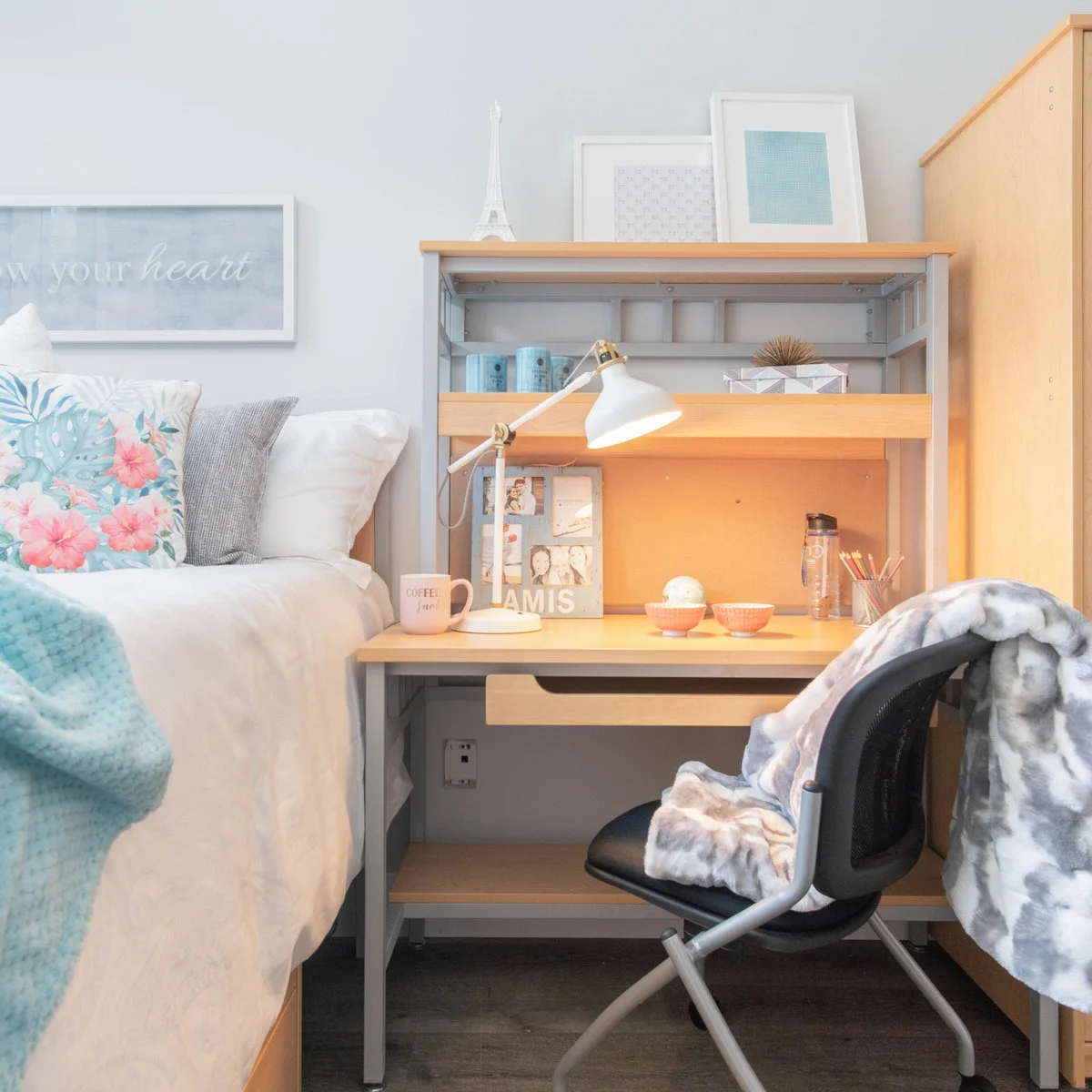 Student desk with a shelf hutch, adjustable white lamp, pencils and notebooks beside a bed with blue accents