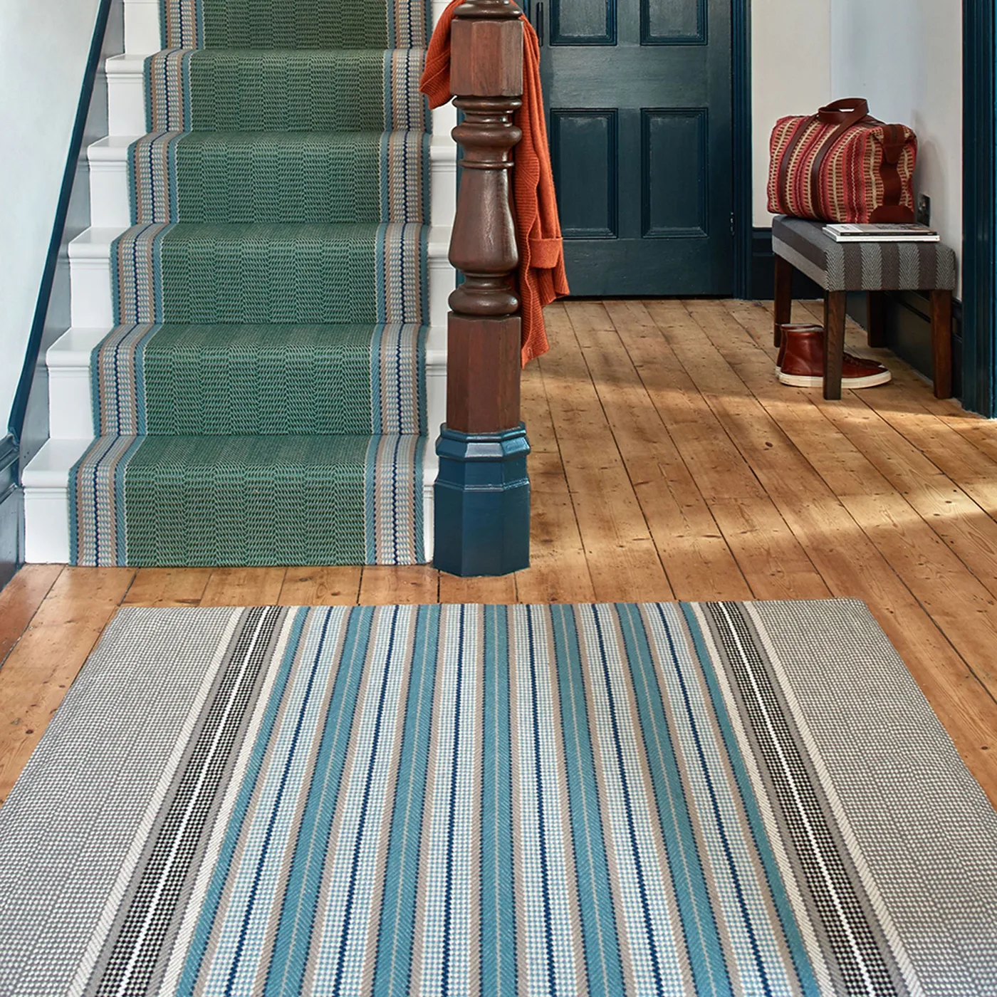 Blue, gray and pale striped hall rug near a dark blue door and green stair runner with contrasting edge bands