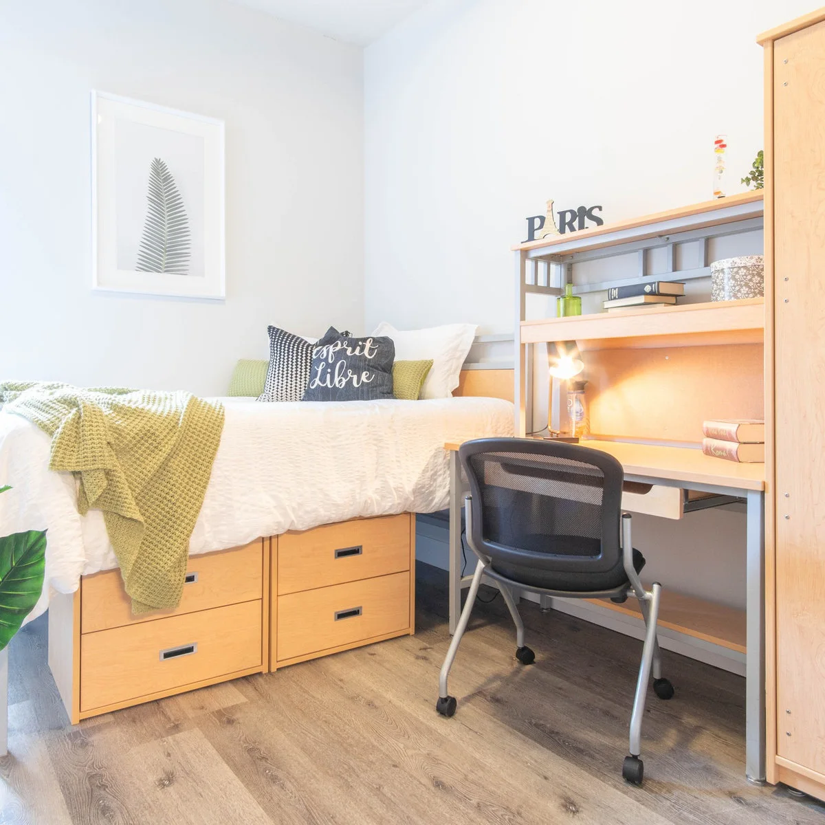 Student bed with white bedding, green knitted throw and under-bed drawers beside a matching desk
