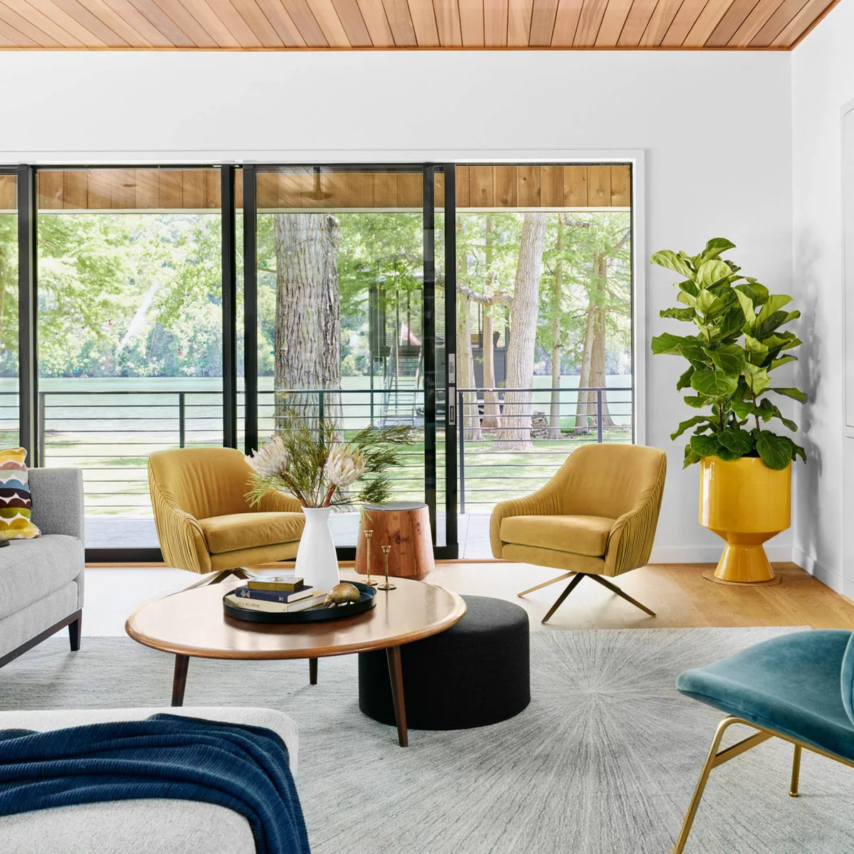 Living room with two mustard chairs, a gray sofa, teal seat and yellow planter beside large glazed doors