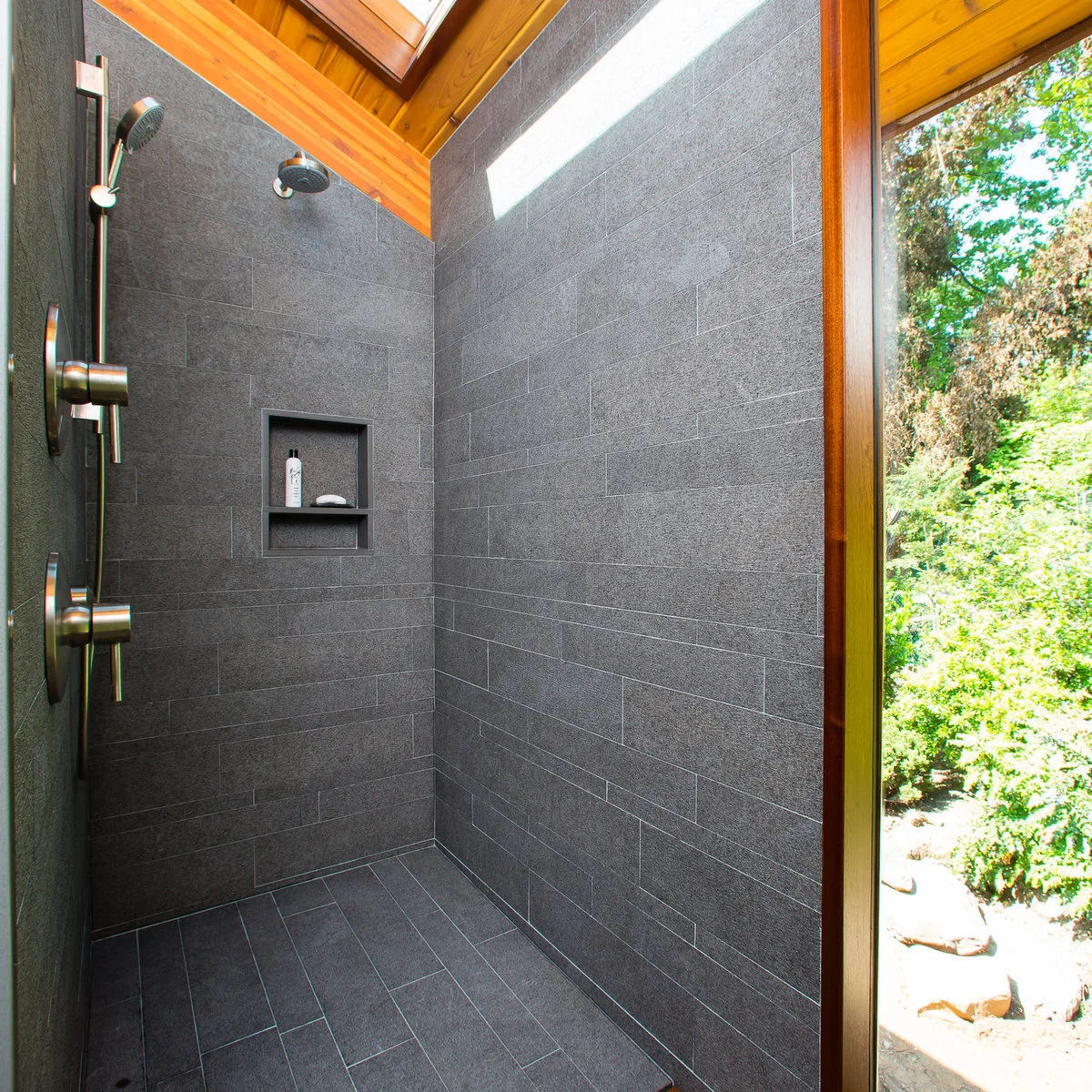 Dark gray tiled shower beneath a wood ceiling with a high narrow window