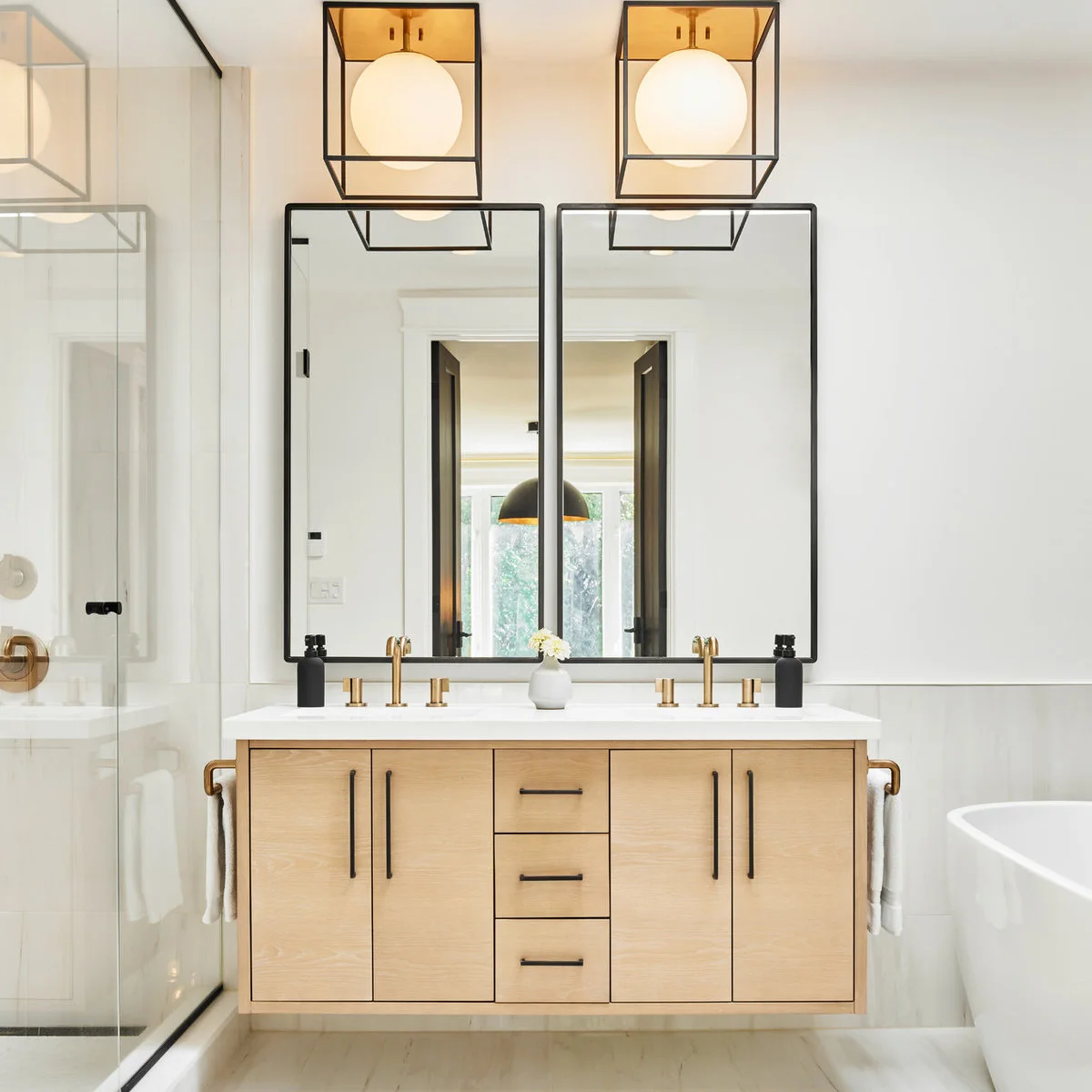 Two short warm-metal towel holders sit on the outer ends of a floating wood double vanity beneath dark-framed mirrors.