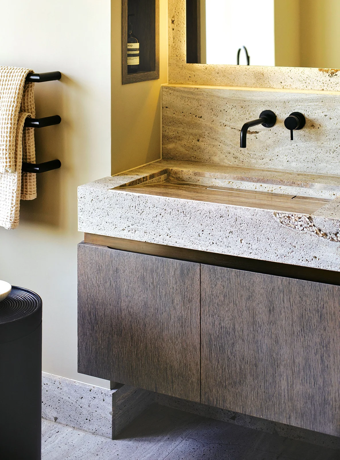 A textured pale basin and backsplash above dark wood cabinet fronts with black wall taps