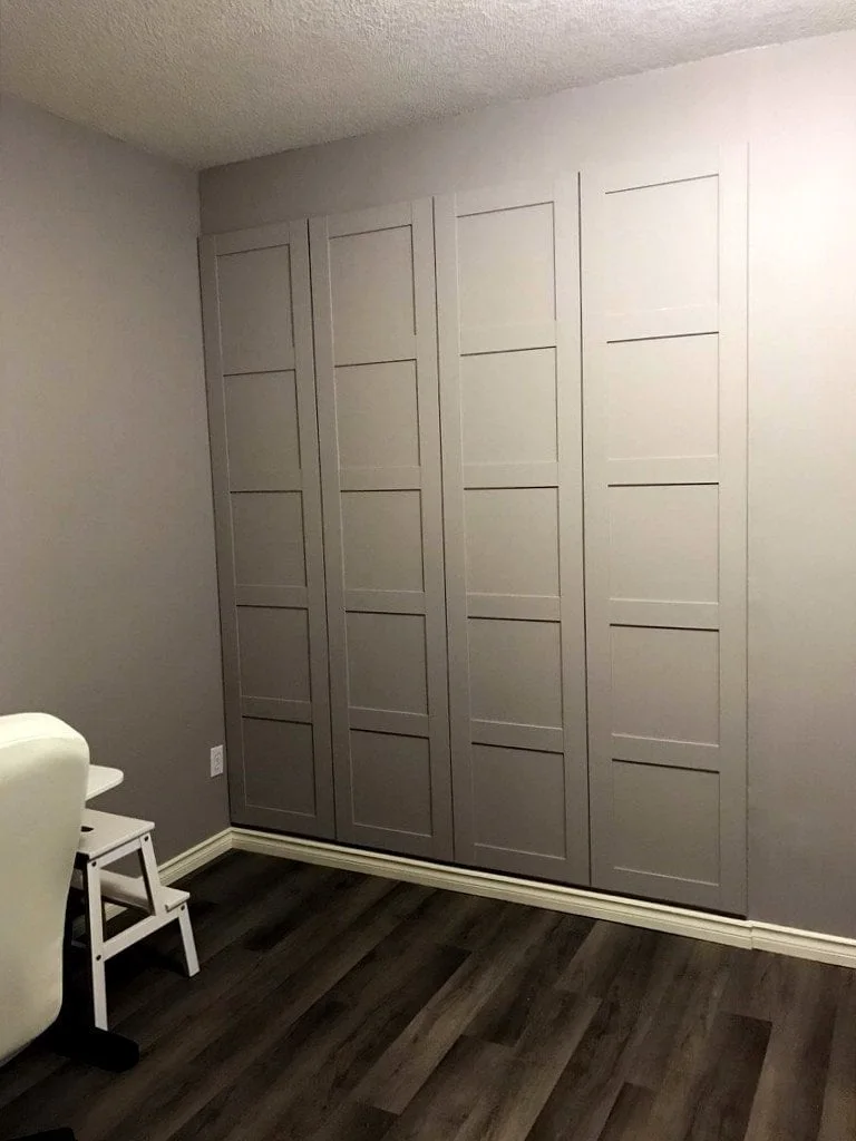 Gray paneled PAX doors fitted into a bedroom recess above dark flooring