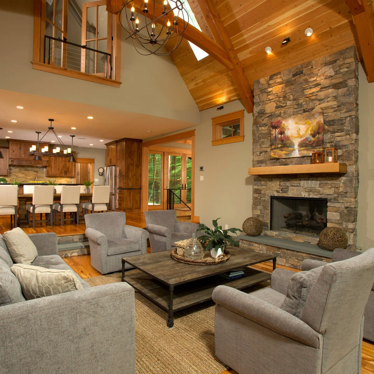A vaulted living room with a stone fireplace, exposed timber framing, gray seating and a broad wood coffee table.