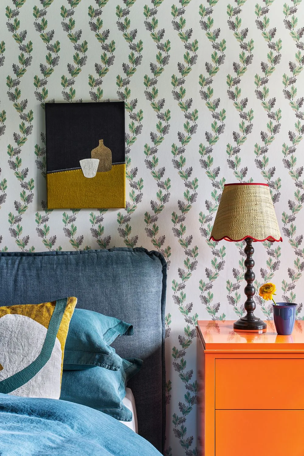 Small flower sprigs on white wallpaper beside a blue headboard and orange bedside cabinet.