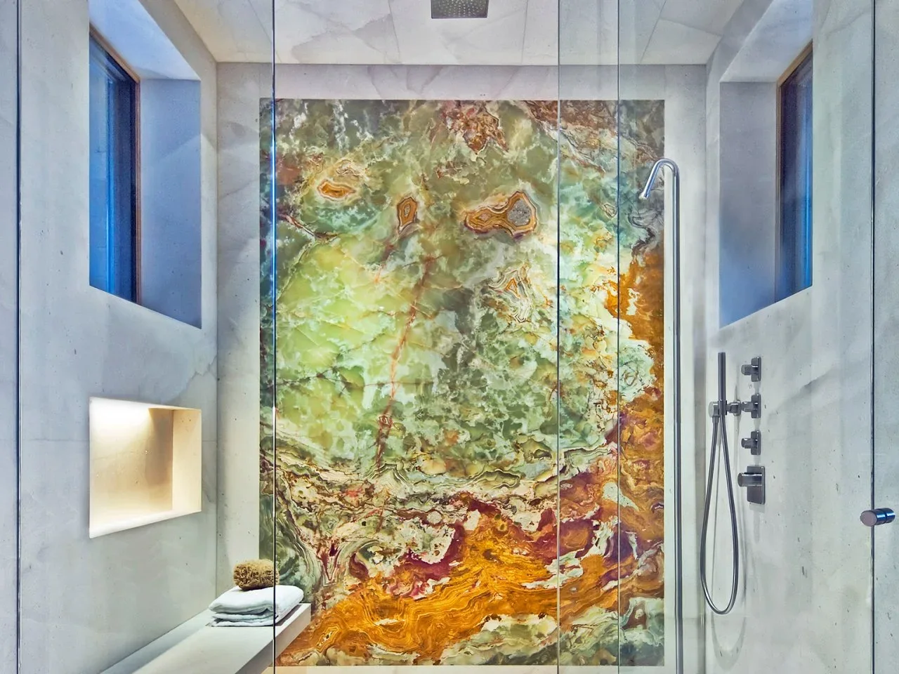A green-and-gold veined feature wall stands behind glass shower doors and pale surrounding tiles.