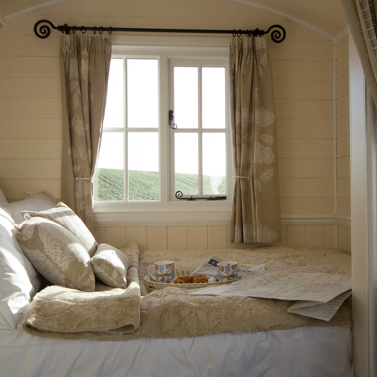 Compact pale wood-lined sleeping space with short curtains and layered cream bedding