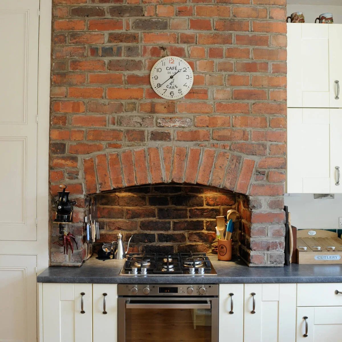 Terraced-house kitchen with exposed brick chimney breast, an inset cooking area and white cabinets