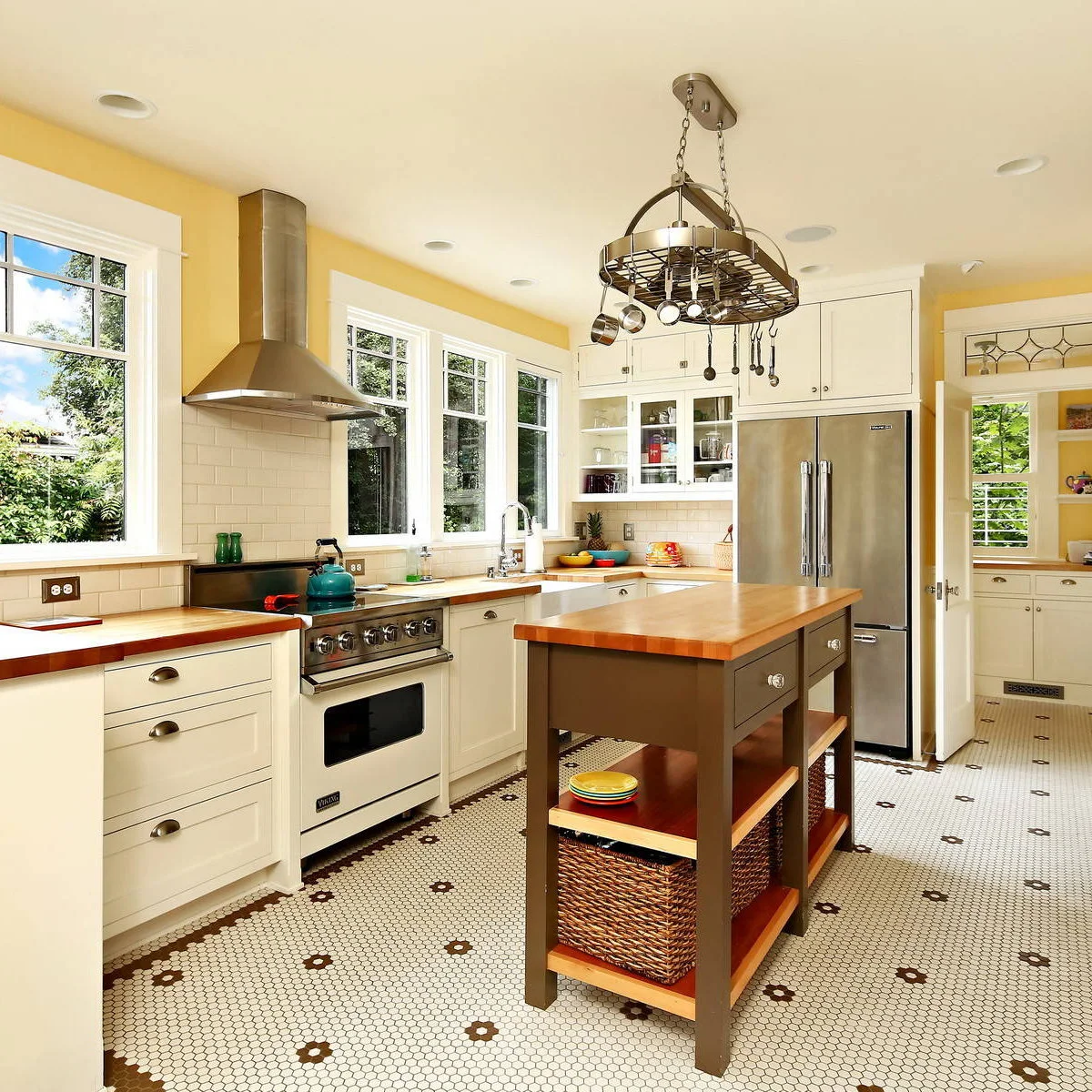 Yellow kitchen walls surrounding white cabinets, a dark island and a hanging pot rack