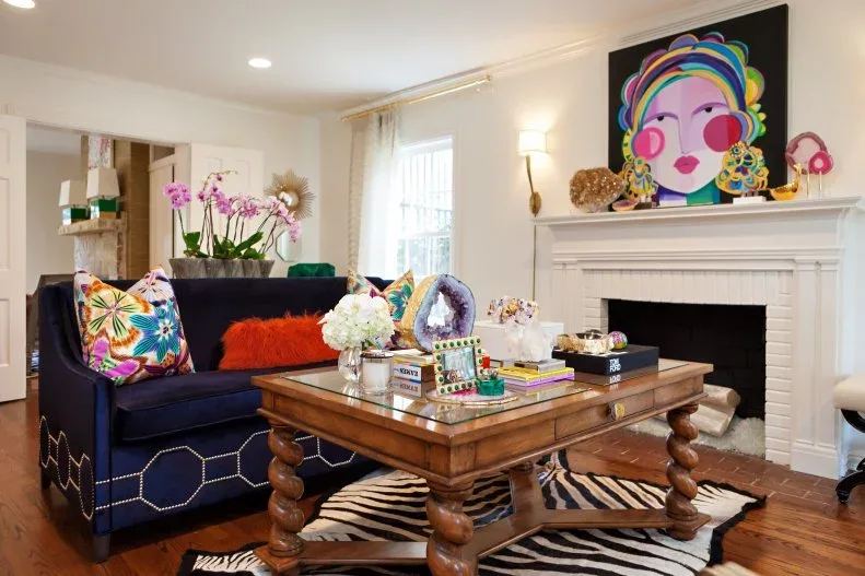 Dark sofa, colorful portrait over a white fireplace, turned-leg wooden table and zebra-patterned rug.