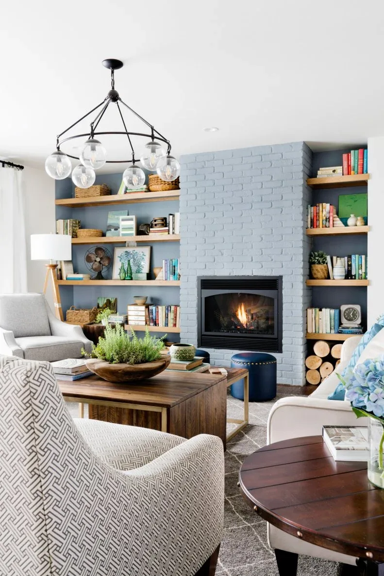 Pale gray brick chimney with warm wood alcove shelves holding books and baskets beside pale chairs