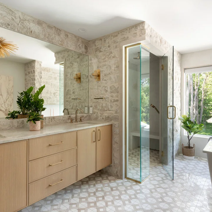 Light wood vanity drawers and a glass shower sit beside patterned pale walls, a geometric floor and a broad mirror.