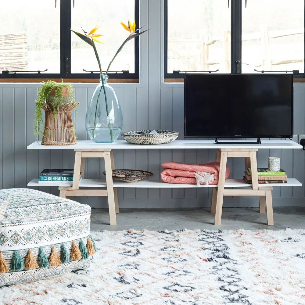 Low media stand with two light wooden stools supporting white horizontal shelves beneath a television