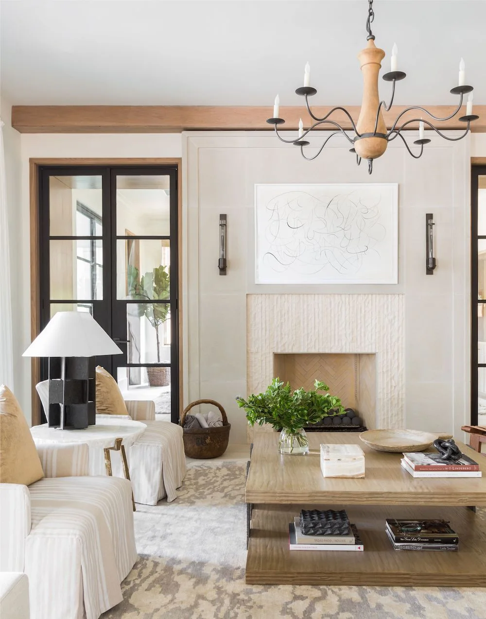 A pale textured fireplace surround sits between tall dark-framed windows beneath a timber beam.