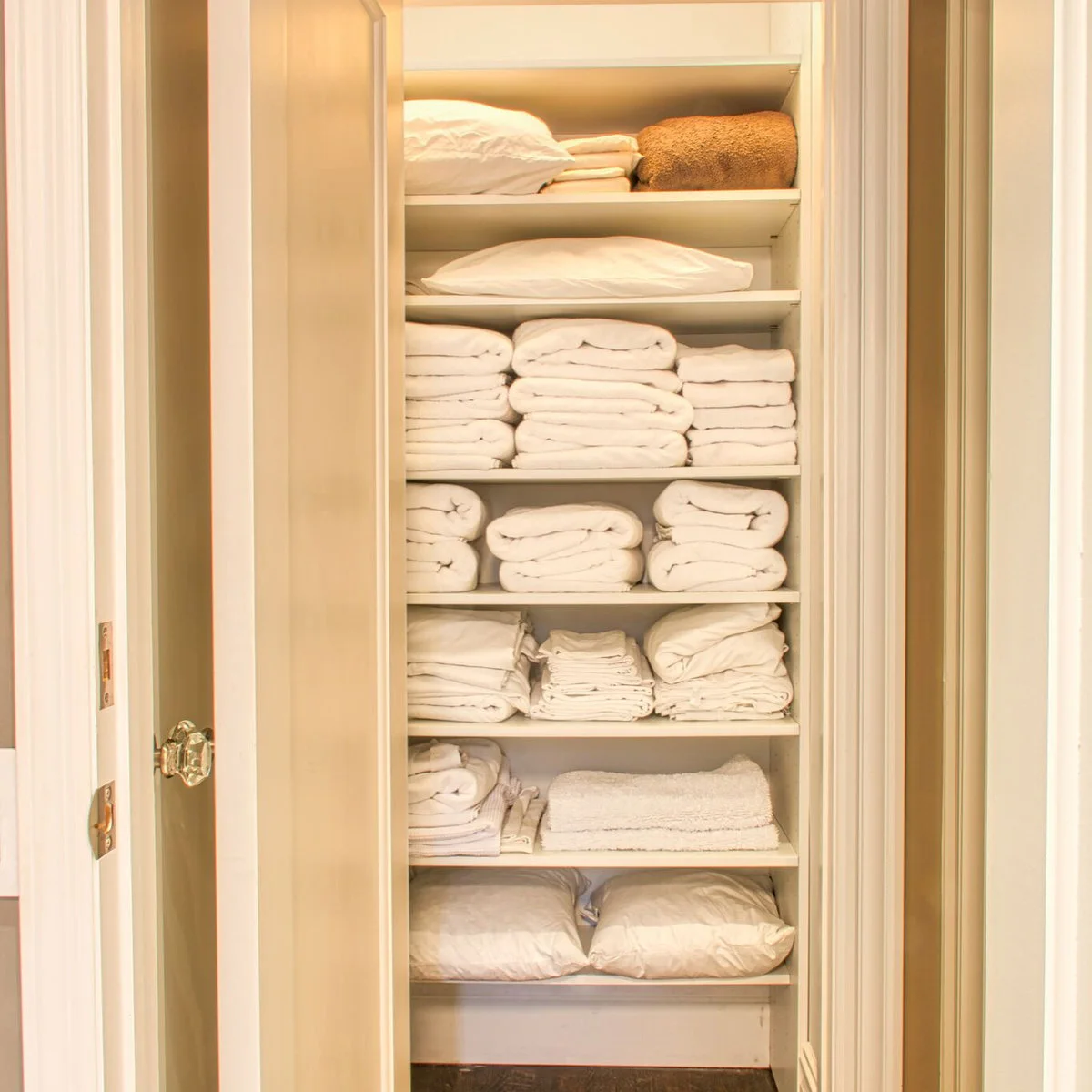 Slim white closet filled with separate stacks of towels, sheets and spare pillows