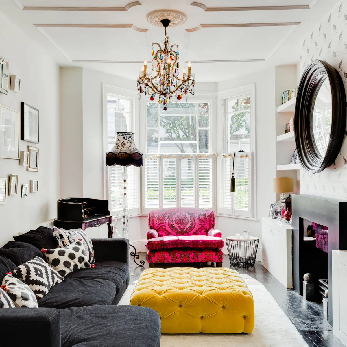 Dark corner sofa with monochrome cushions beside a yellow ottoman and bright pink chair