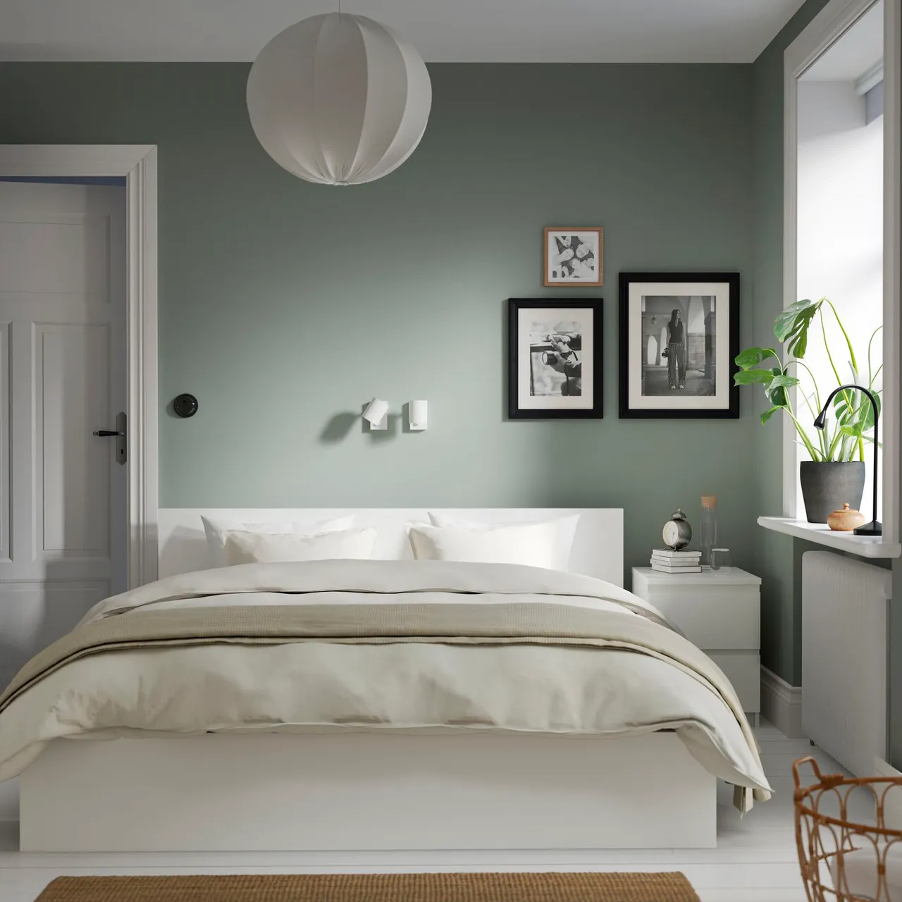 A pale bed sits against muted green walls beneath a paper-like pendant.