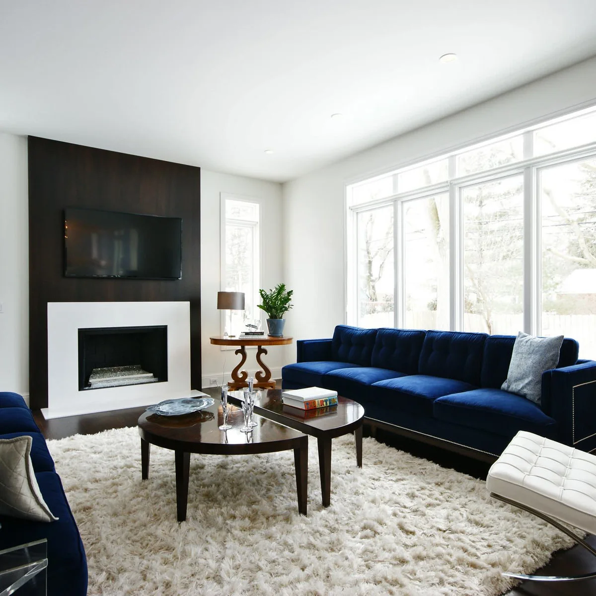 A navy sofa, pale chair and second navy seat surround two rounded dark coffee tables on a white rug.