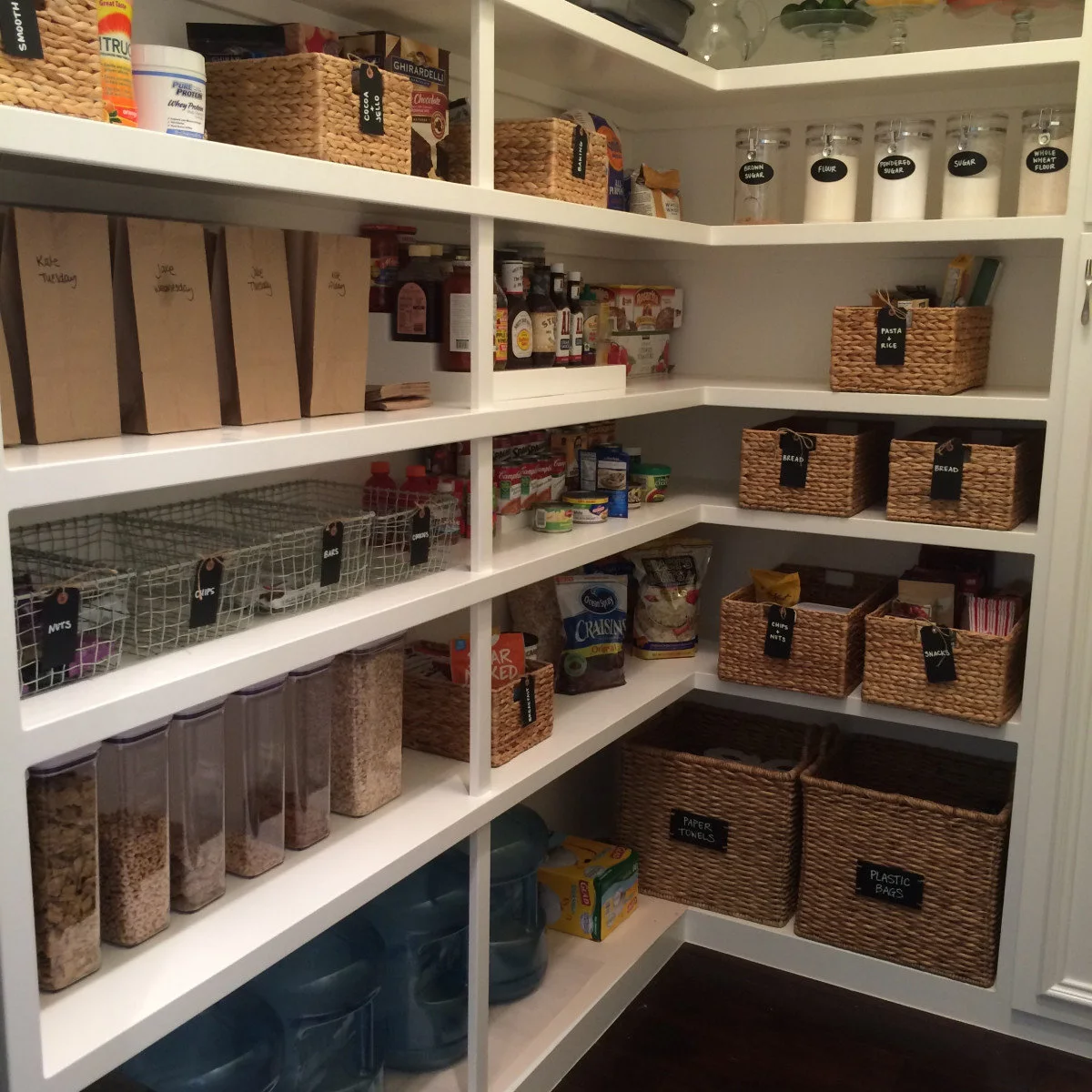 White pantry shelves with labeled baskets, wire bins and clear dry-food containers