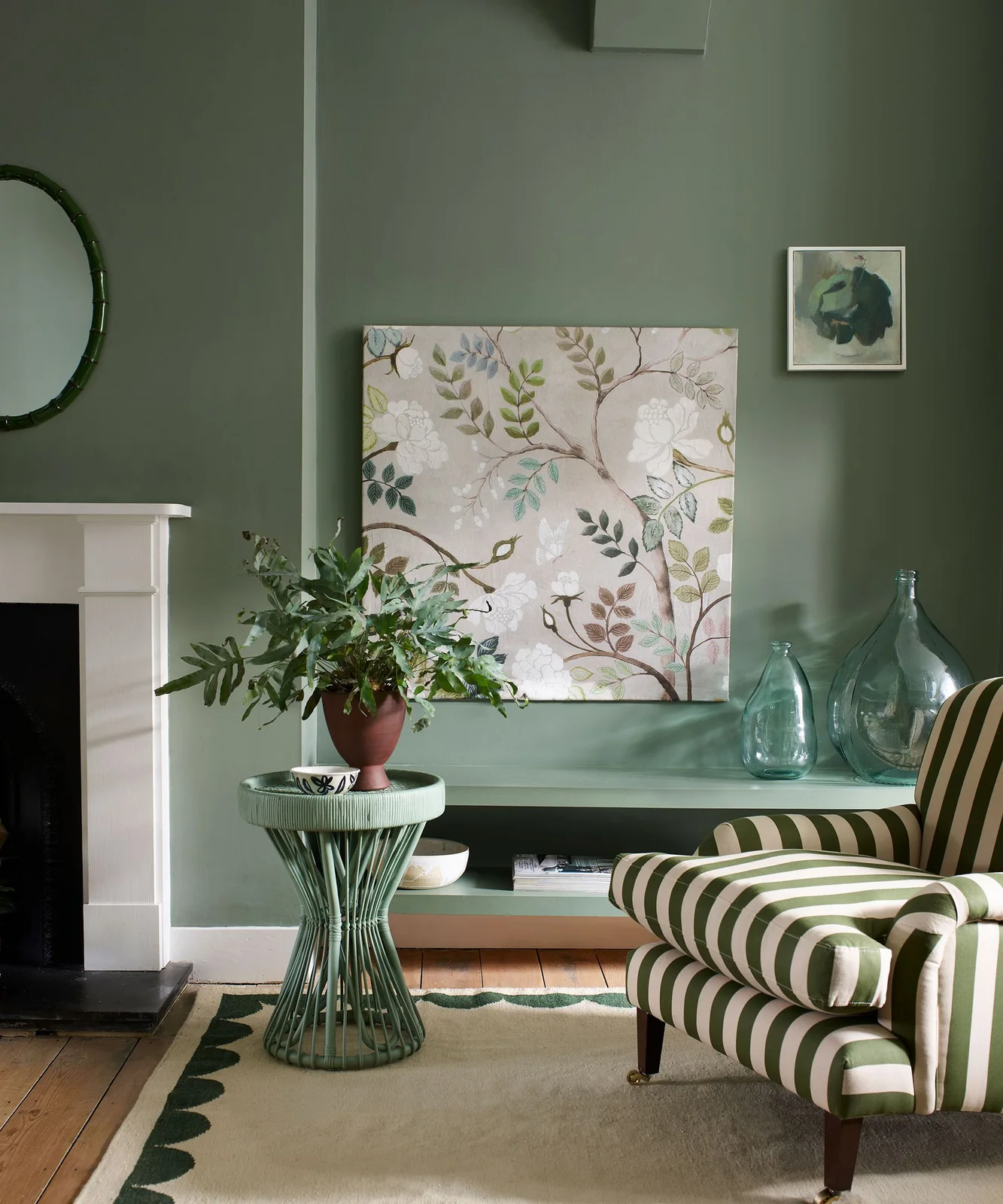 A green-and-pale striped armchair sits beside a green side table and low shelf against gray-green walls