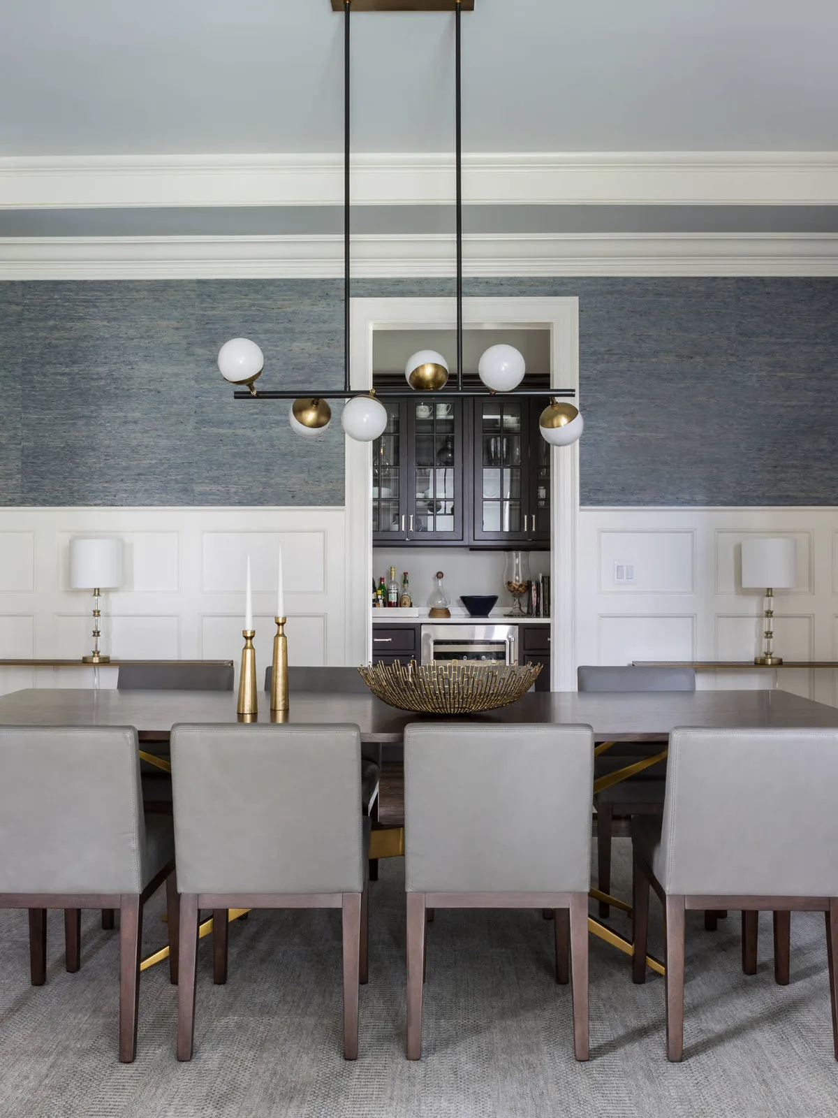 Gray textured wallpaper above white paneling behind pale dining chairs and a long table