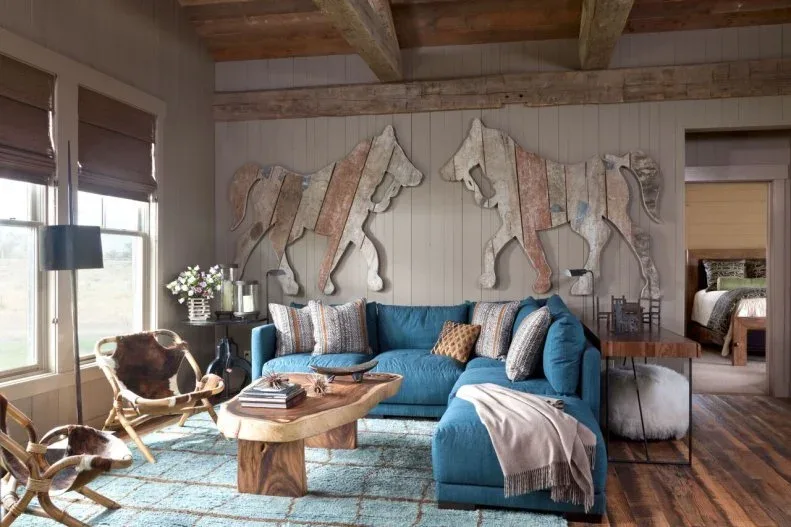 Timber-framed room with blue sectional, large horse-shaped wood wall decorations, irregular wood table and patterned cushions