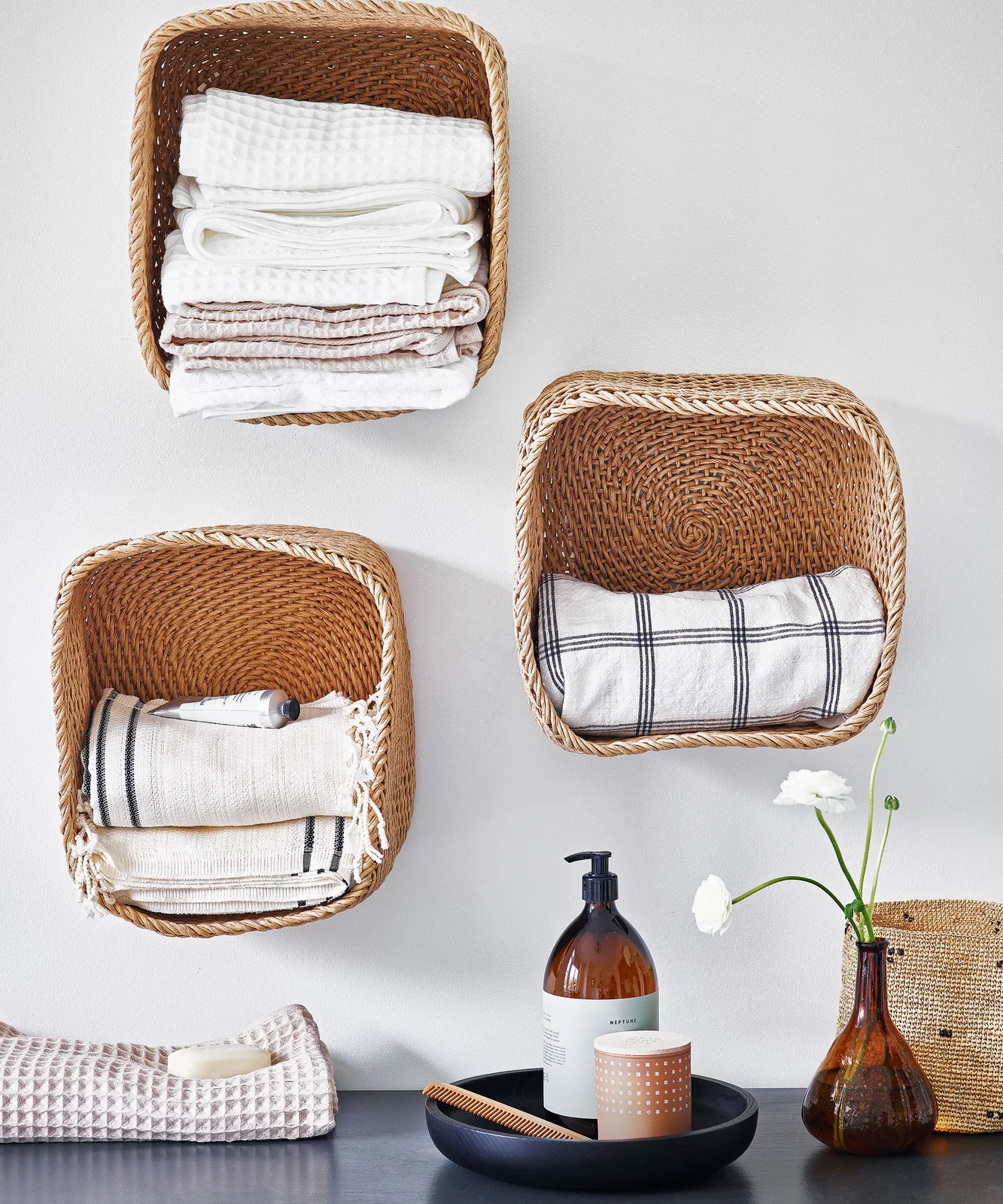 Three woven baskets fixed to a wall holding folded bathroom towels