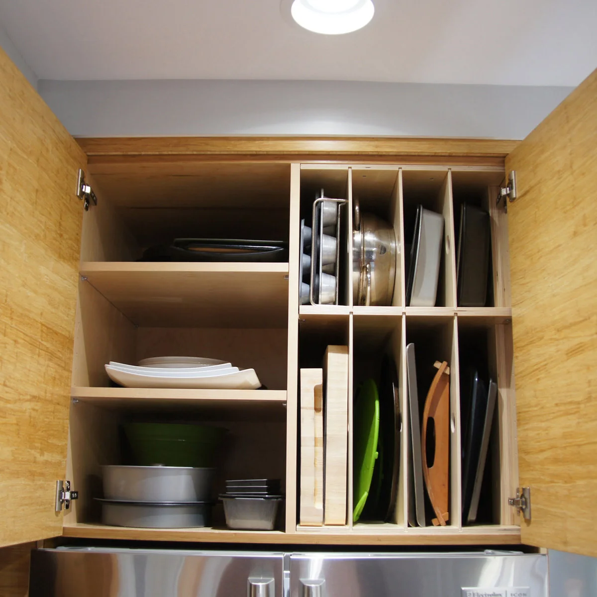 A wood cabinet above a refrigerator combines adjustable shelves with two rows of vertical tray compartments.