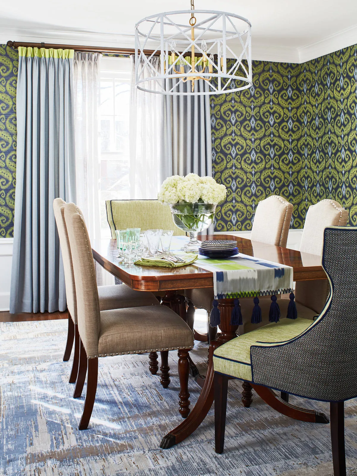 Green patterned wallpaper behind a warm timber dining table with pale and green upholstered chairs