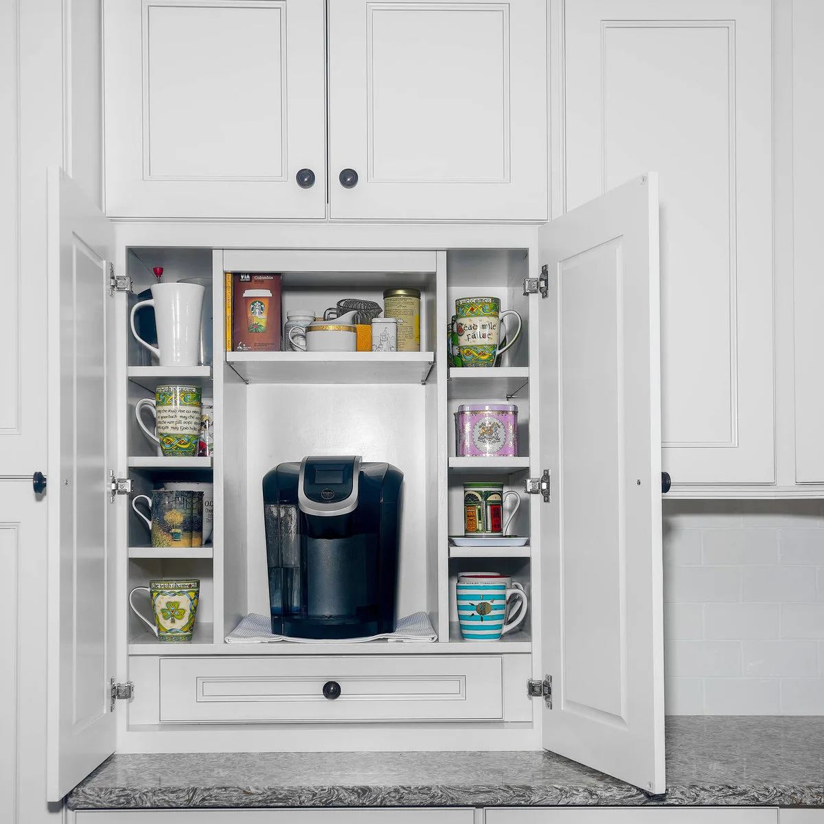 White coffee cupboard with narrow mug cubbies on both sides of a black machine