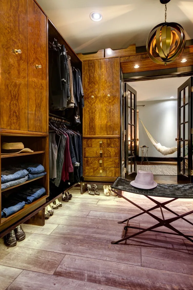 Figured timber closet cabinets combine hanging rails and folded storage beside a low folding-style bench.