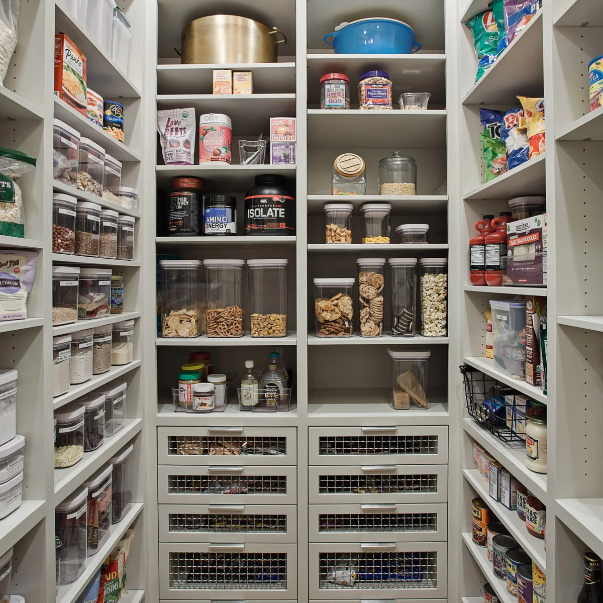 Pantry with clear food containers on adjustable shelves above wire-front drawers