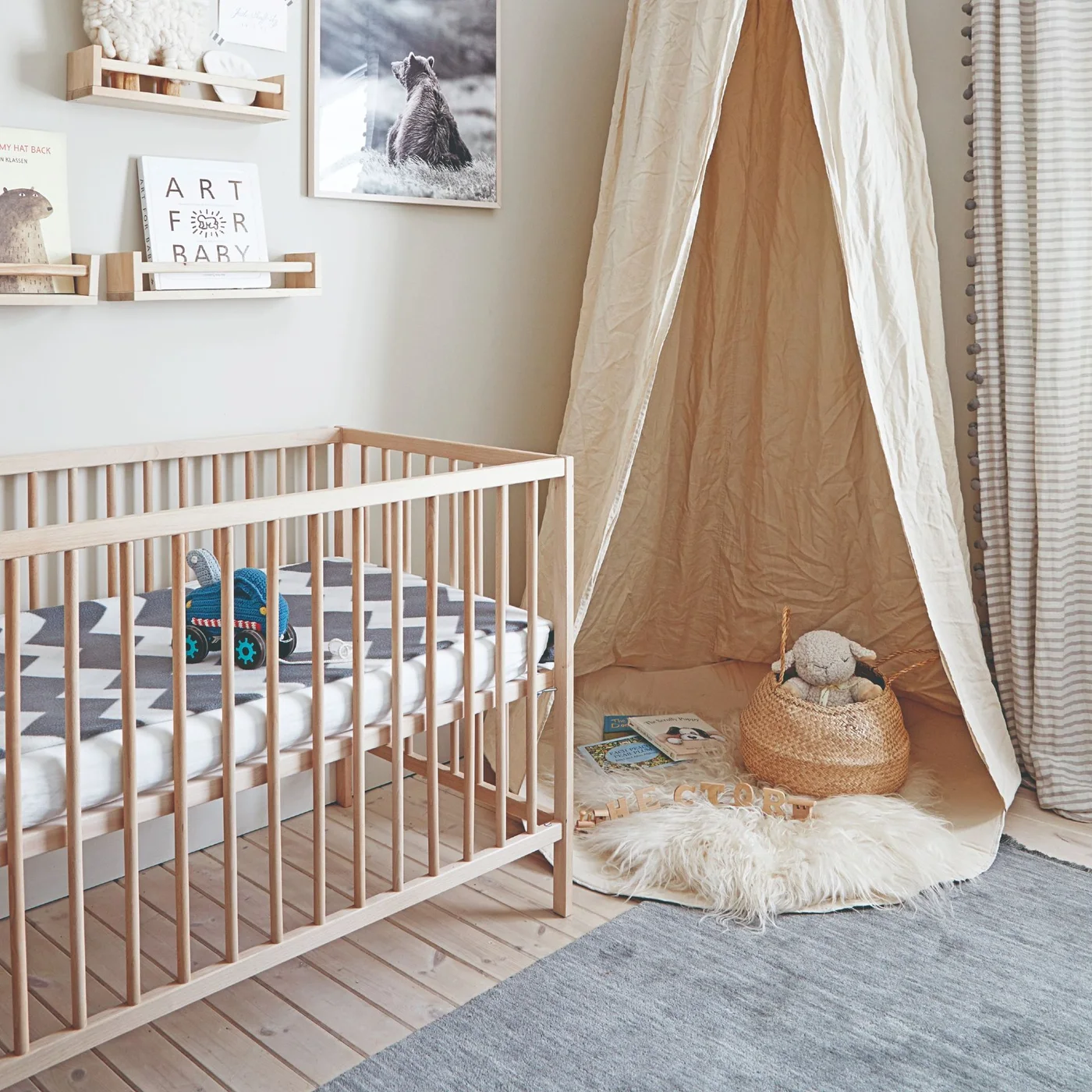 A light wooden crib sits beside narrow book ledges and a fabric play corner in a pale nursery