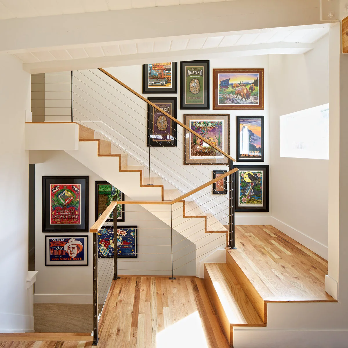 White turning staircase beside a gallery of colorful concert and event prints in varied frames