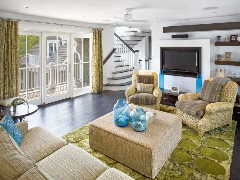 Light sitting room with green patterned chairs, a green rug, blue glass vessels and broad French doors.