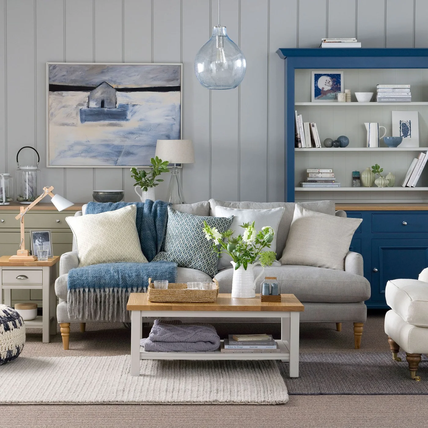 Pale gray vertical paneling and framed art stand behind a pale sofa beside a blue shelving cabinet