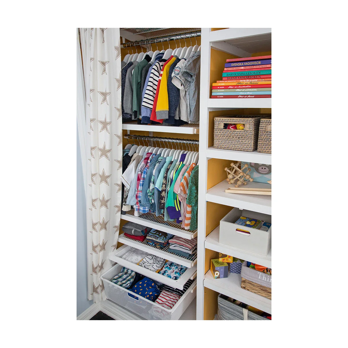 Nursery closet with two short hanging rails, mesh drawers, baskets and yellow-backed shelves