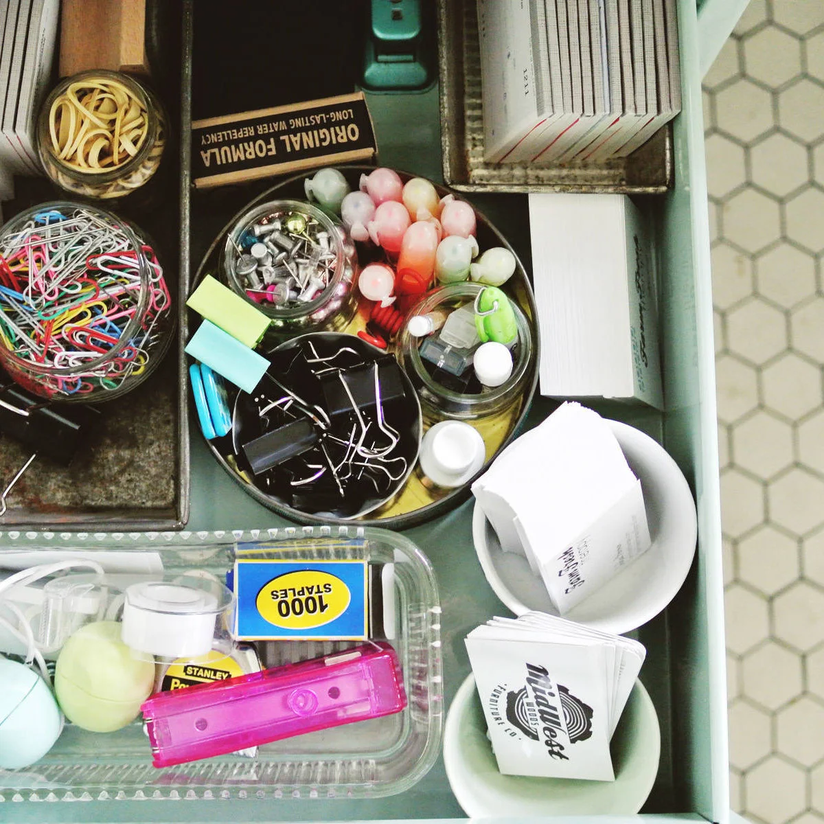 Utility drawer with glass cups, shallow tins, paper clips, binder clips, pens and small paper supplies