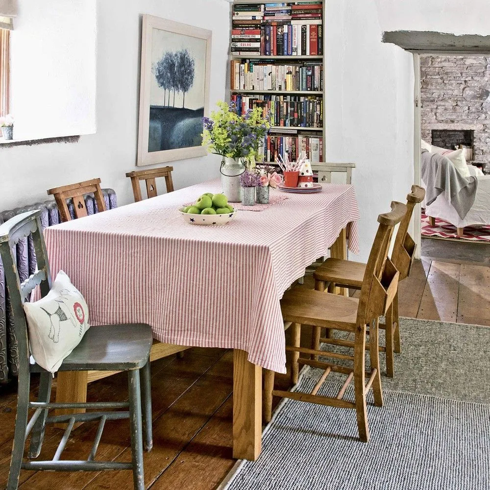 A striped tablecloth covers a wood dining table beside mixed chairs, a tall recessed bookcase and pale walls.