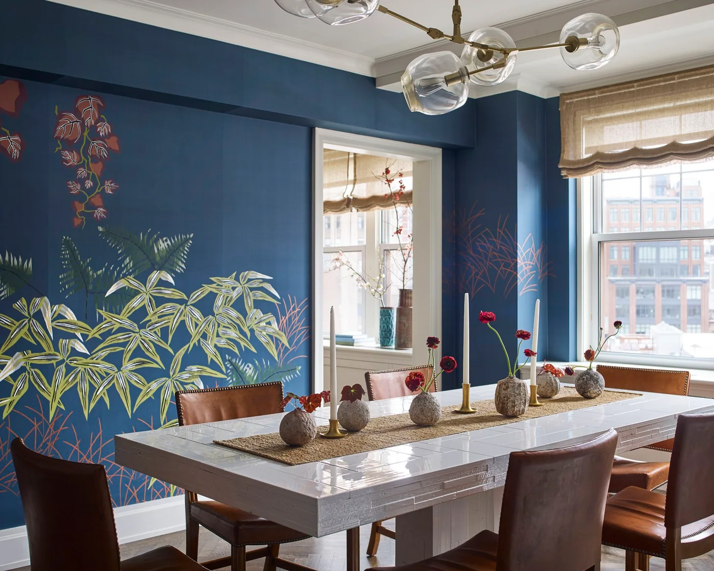 A navy dining-room mural with green and rust leaves sits behind a pale tiled table and brown upholstered chairs.