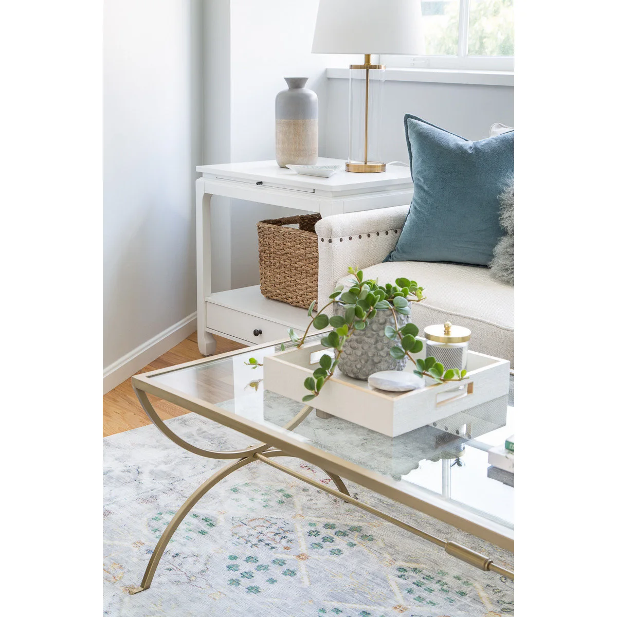 White side table with a basket beneath it beside pale upholstery and a glass coffee table