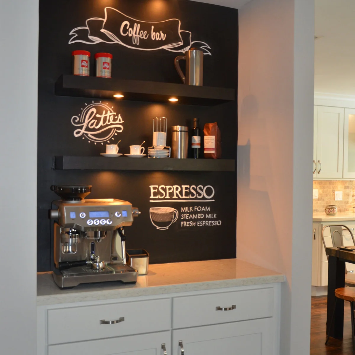 Recessed coffee bar with black chalkboard backing, lit shelves and an espresso machine