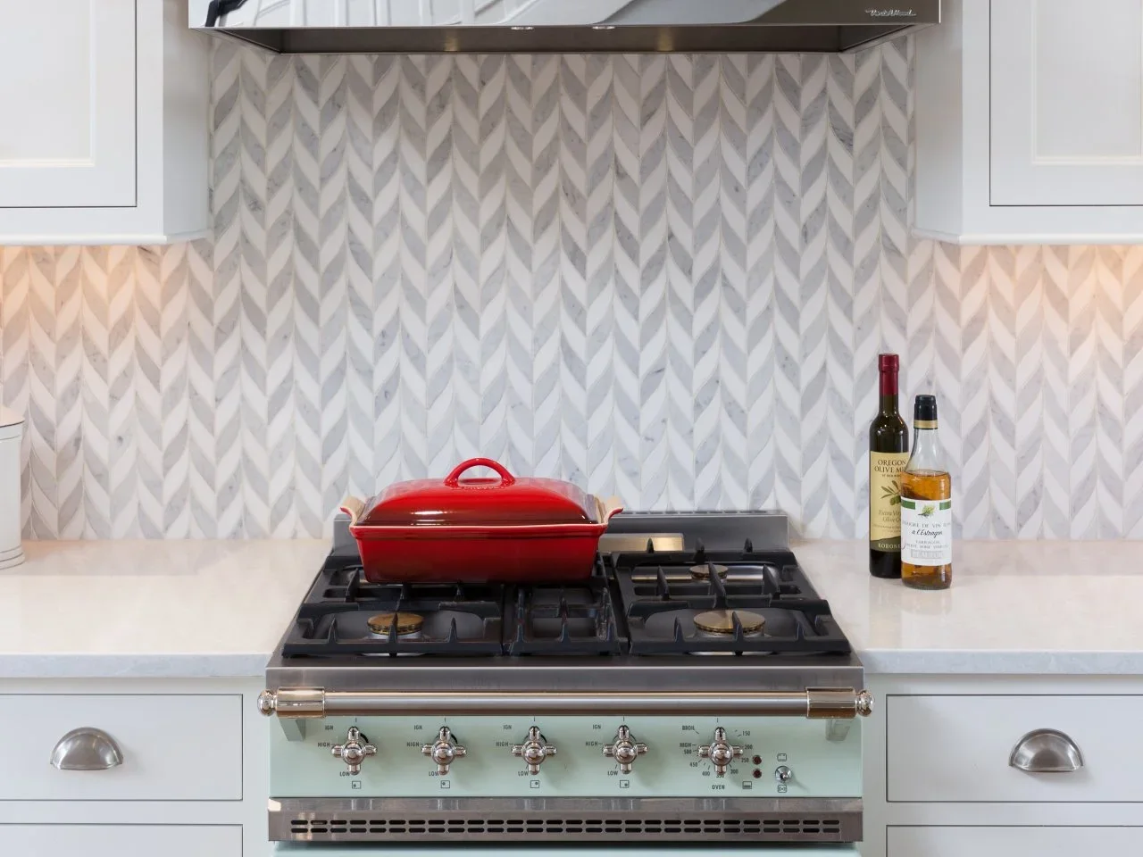 A gray-and-white patterned tile backsplash sits above a pale teal range beneath a metal hood.