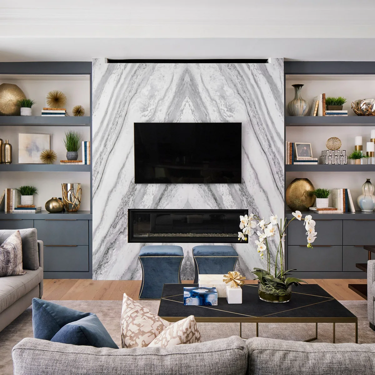 A television and narrow fireplace on a boldly veined pale wall between blue-gray shelves and cupboards.