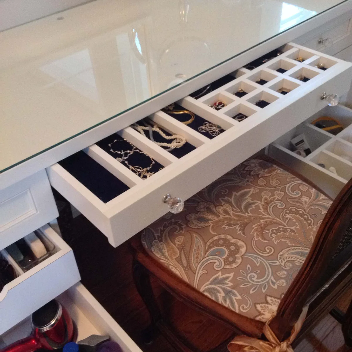 Open shallow vanity drawers contain divided compartments holding necklaces and small jewelry pieces